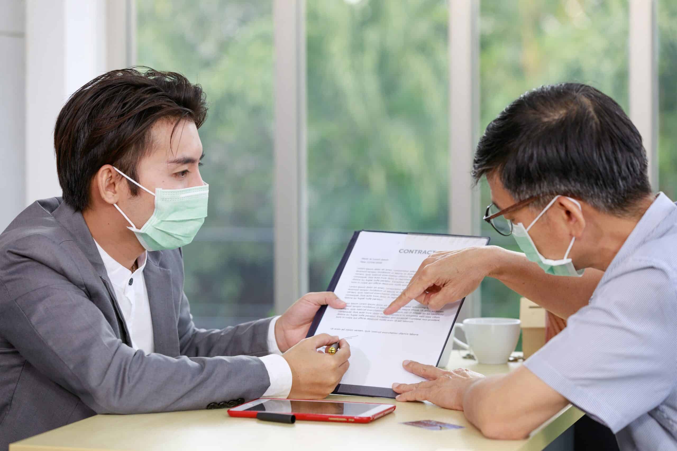 A close-up image of an adult's hand signing a contract in a workplace setting.