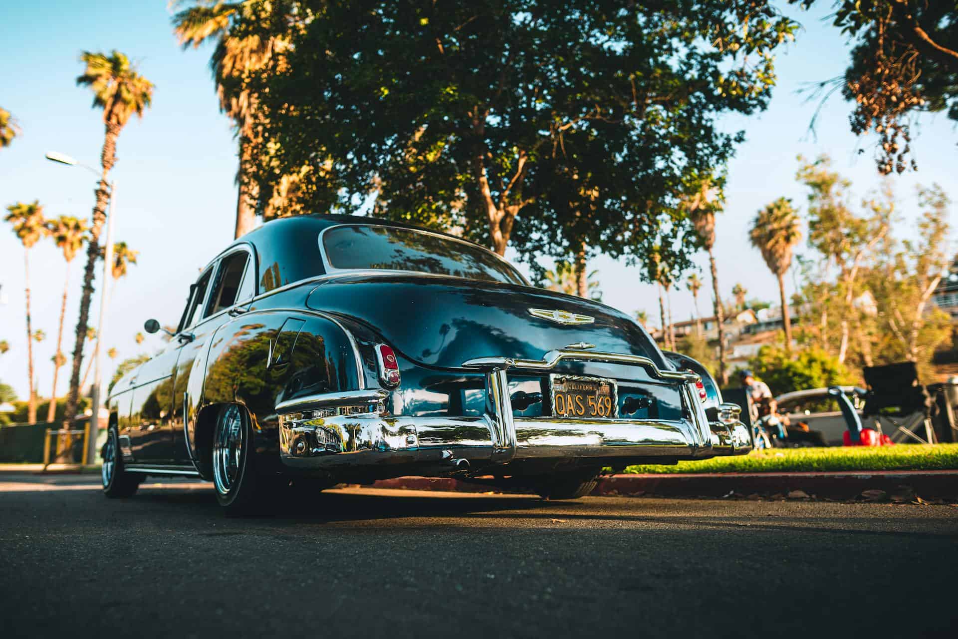A classic car parked on a street with palm trees in the background